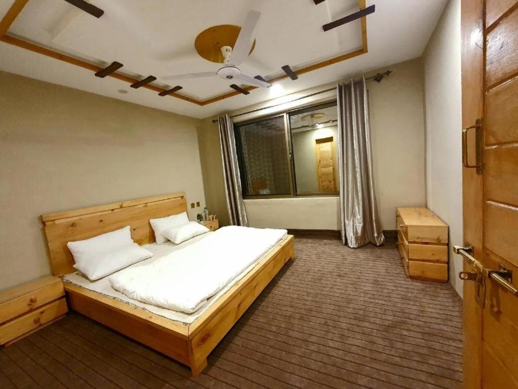 Queen bed with seating area in Skardu guest house, interior view of HIKK Inn Skardu room
