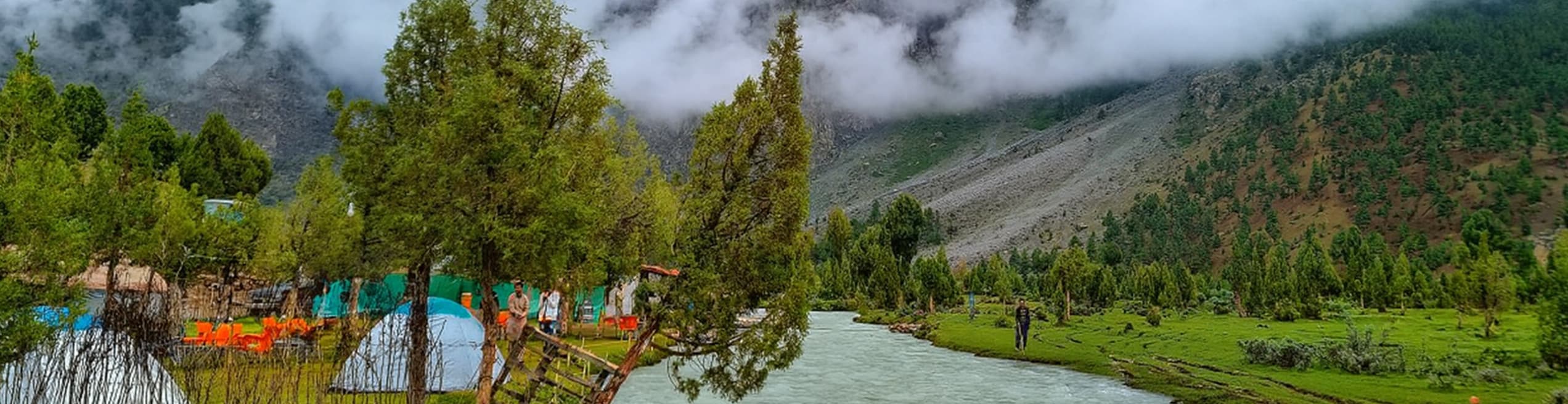 Scenic Riverside Campsite in Basho Valley Beautiful riverside campsite in Basho Valley, with tents set along a flowing river and surrounded by green meadows and mountains.
